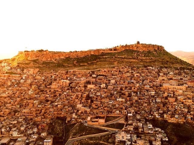 Gün batımında kale kayasının eteğine yayılan Eski Mardin'in bal rengi evleri